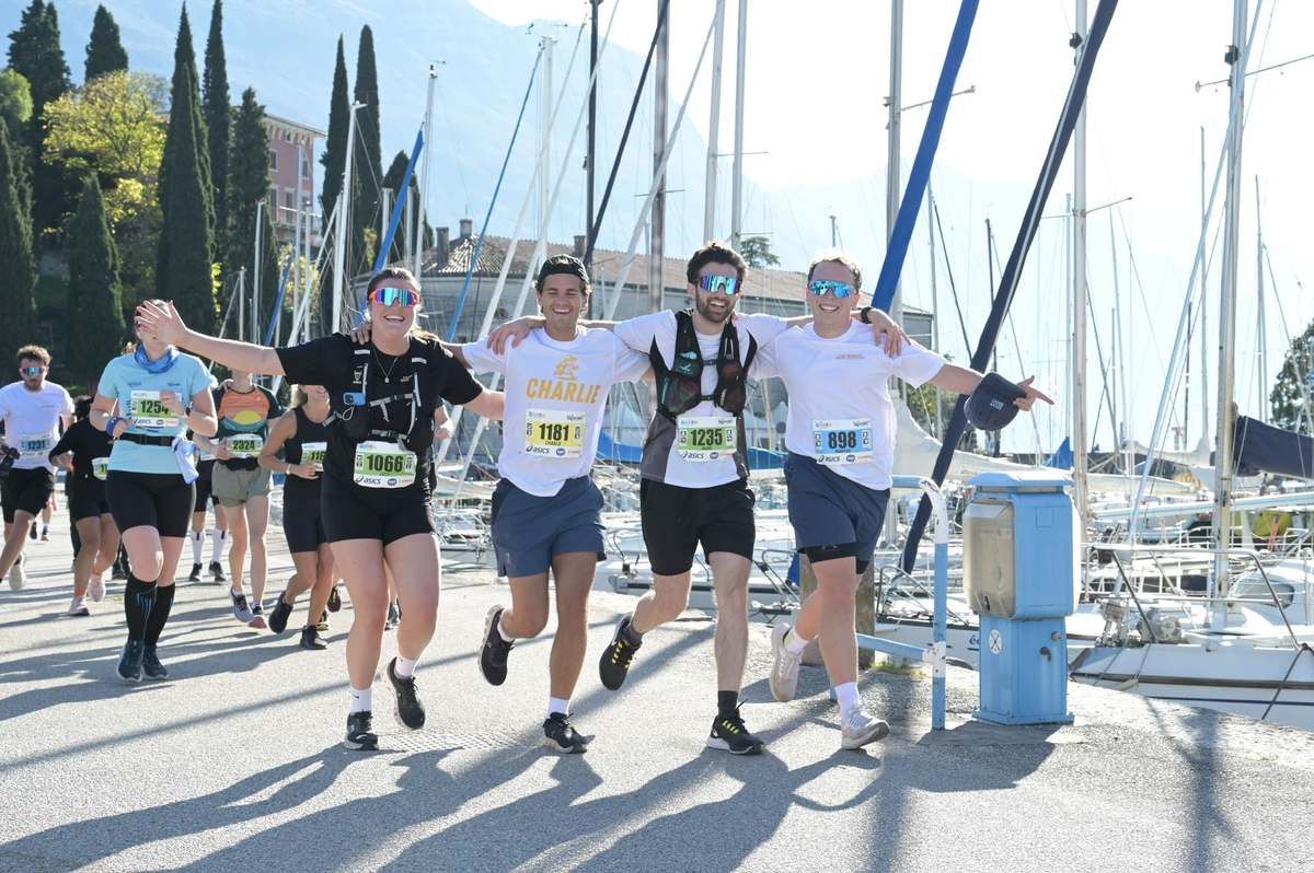 Four runners with arms linked celebrating together by a marina in Lake Garda
