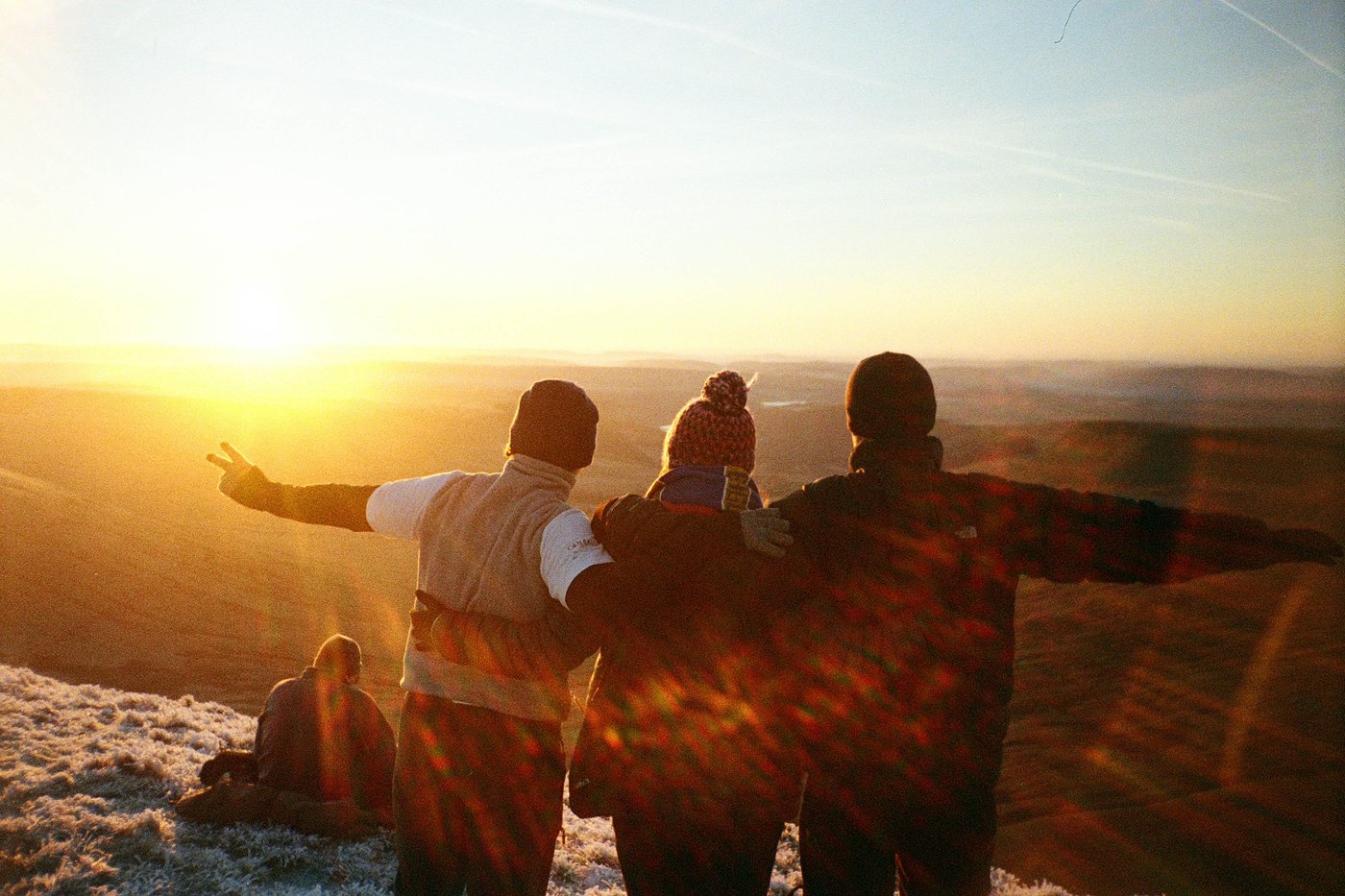 Three friends with arms around each other looking out at a sunrise