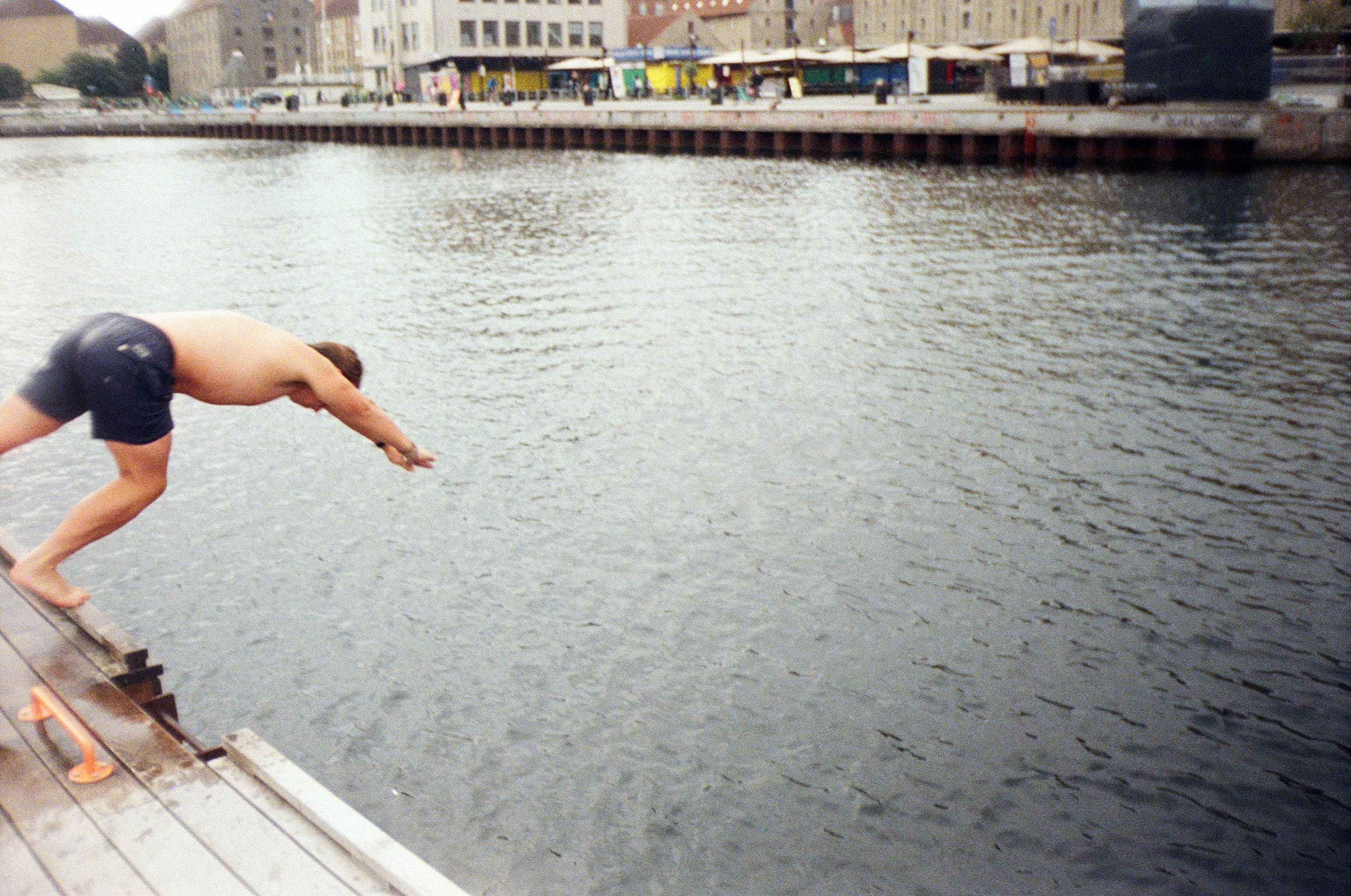 A swimmer diving off a wooden jetty into a city harbour